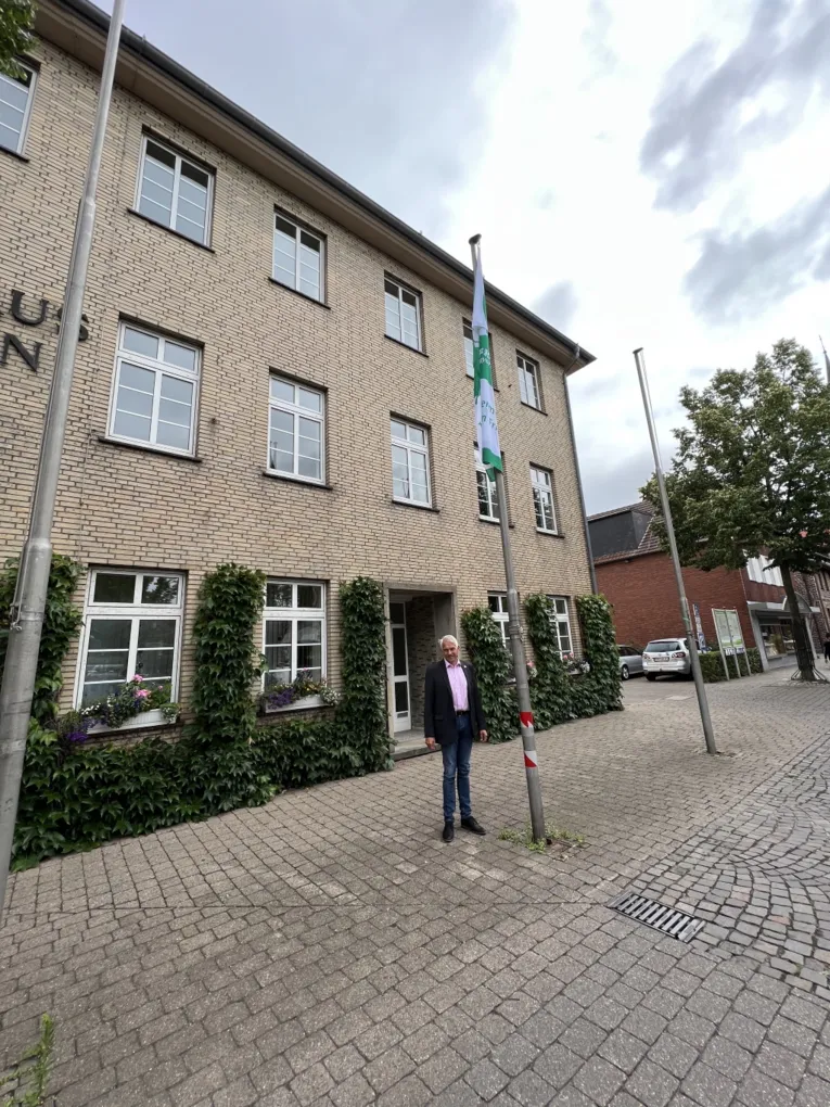 Ein Mann steht neben einem Flaggenmast mit der Mayors-for-Peace-Flagge.